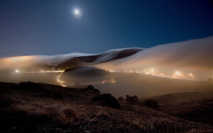 Foggy night landscape with moonlight and city lights