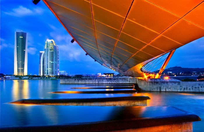 Modern bridge over water with city skyline at dusk