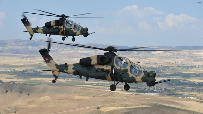 Two T-129 ATAK helicopters flying over a landscape