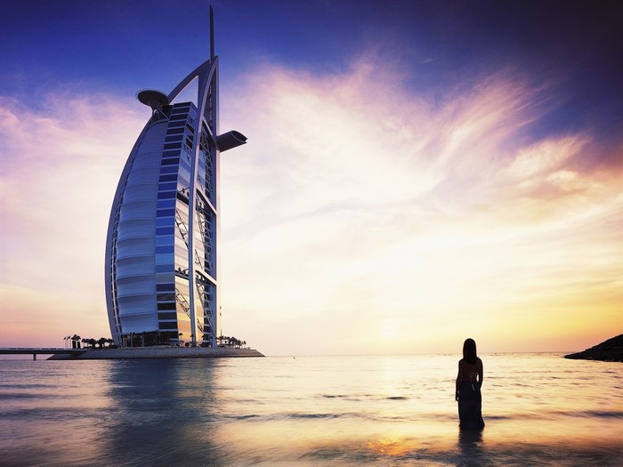 Burj Al Arab hotel at sunset with a woman on the beach