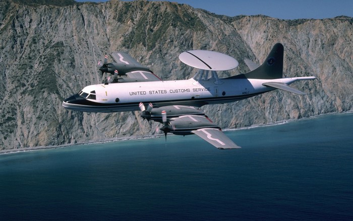 US Customs EP-3 aircraft flying over the ocean near a cliff