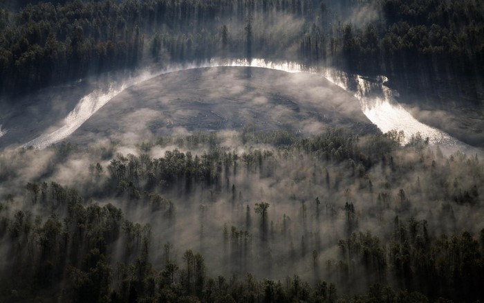 Aerial view of a misty forest with a sunlit river