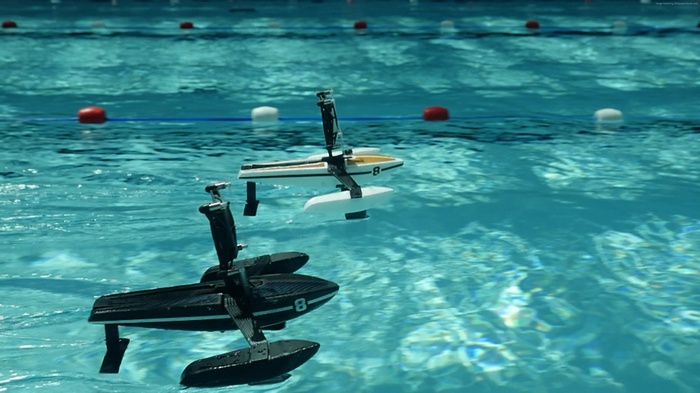 Two remote-controlled hydrofoil boats race in a swimming pool