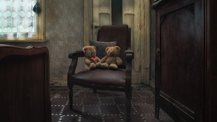 Two teddy bears sitting on a chair in an abandoned room