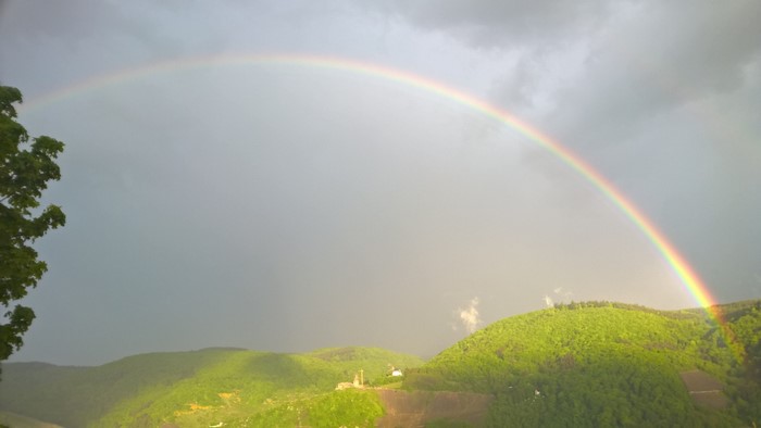 Rainbow over green mountains under a cloudy sky