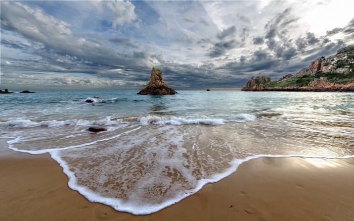 Rocky coast with waves crashing on a sandy beach under cloudy skies
