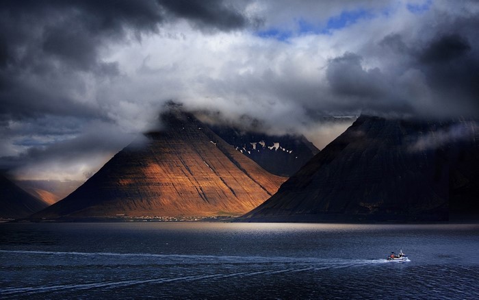 Boat sailing in a fjord with mountains and clouds