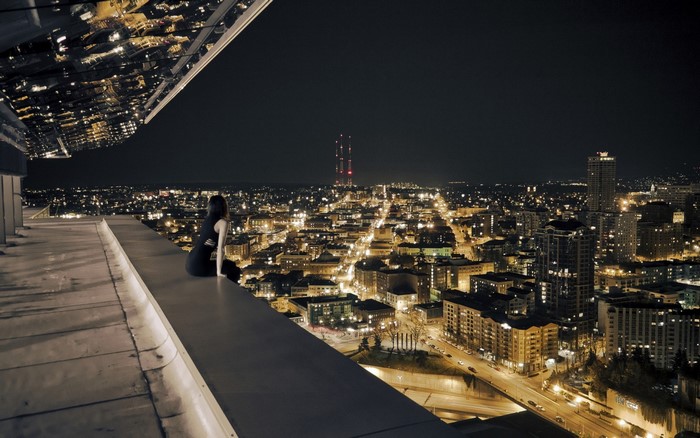 Woman sitting on a rooftop overlooking a city at night