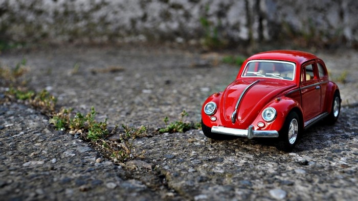 Red Volkswagen Beetle toy car on cracked asphalt