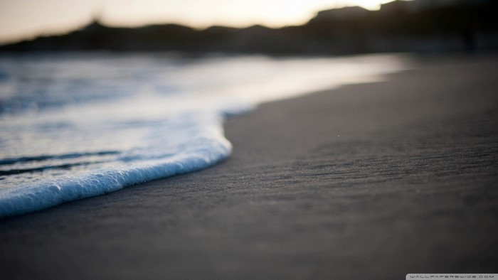 Ocean wave washing onto a sandy beach at sunrise