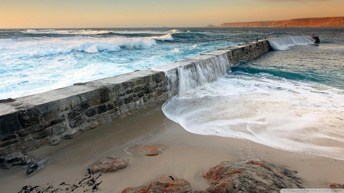 Waves crashing over a stone breakwater on a sandy beach