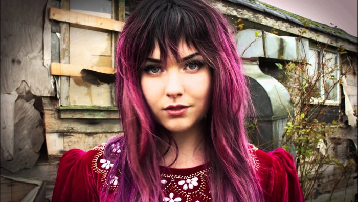 Woman with purple hair in front of abandoned building
