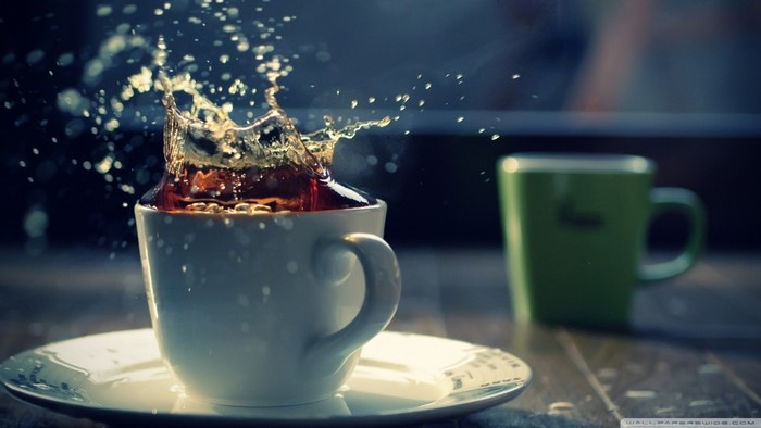Coffee splash in a white cup with a green cup in the background