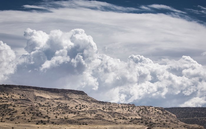 Cumulus clouds over a desert plateau with sparse vegetation