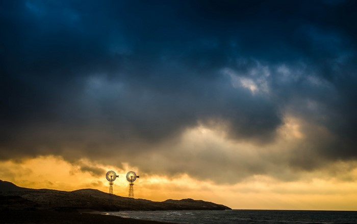 Two windmills on a coast at sunset with stormy clouds