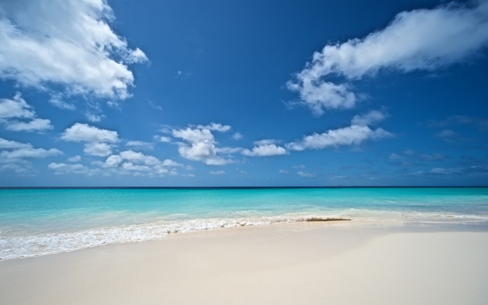 Turquoise ocean waves on a white sand beach under a blue sky