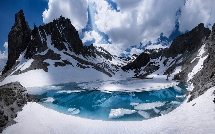 Partially frozen lake in the Alps with snowy mountains