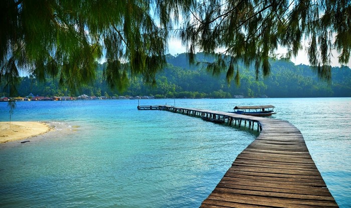 Wooden pier extending into a tropical bay with lush green hills