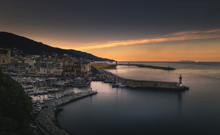 Coastal town harbor at sunset with a ferry and lighthouse