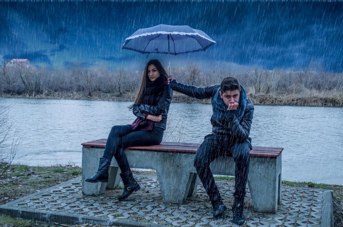 Couple sharing an umbrella in the rain by a lake