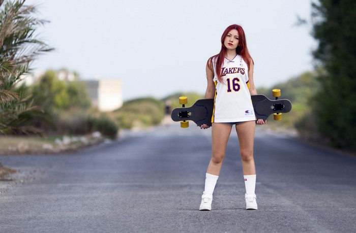 Woman in Lakers jersey holding a skateboard on a road