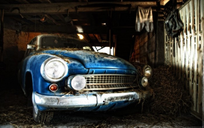 Old blue car covered in hay in a barn