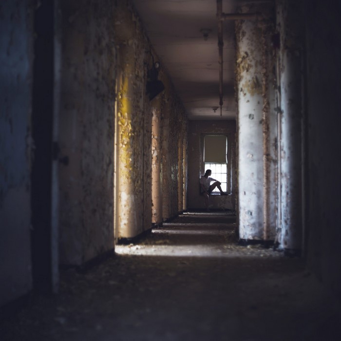 Woman sitting by a window in a derelict hallway