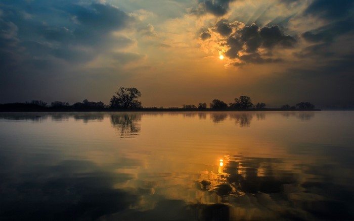 Sunrise over a calm lake with trees on the horizon