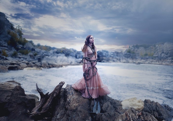 Woman tied with chains on rocks by the sea