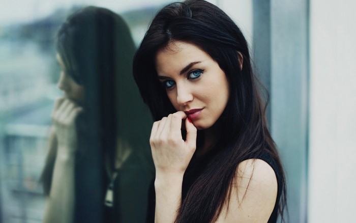 Woman with blue eyes and black hair reflected in glass