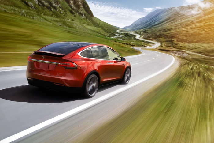Red Tesla Model X driving on a winding mountain road