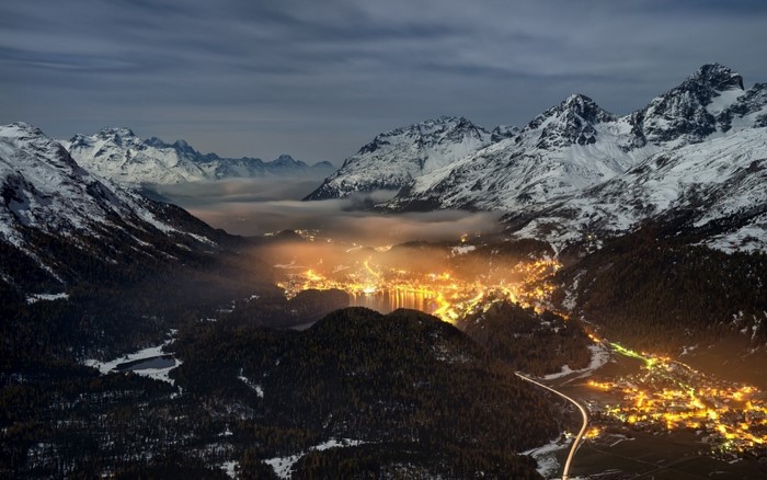 Valley town lights at night with snowy mountains