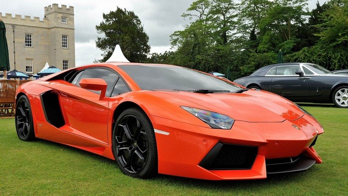 Orange Lamborghini Aventador parked on grass with castle in background