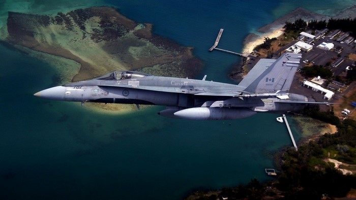 Canadian F/A-18 Hornet flying over tropical coastline