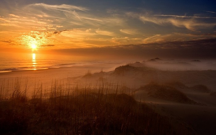 Sunset over a misty beach with sand dunes and ocean waves