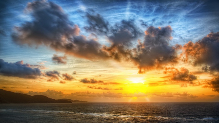 Sunset over the ocean with clouds and mountains