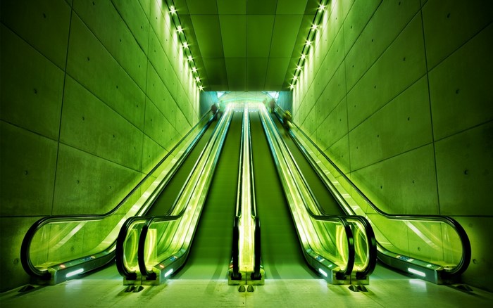 Green escalators in a concrete tunnel with lights