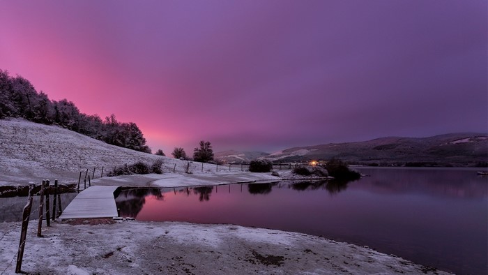 Snowy landscape with lake and purple sunset sky