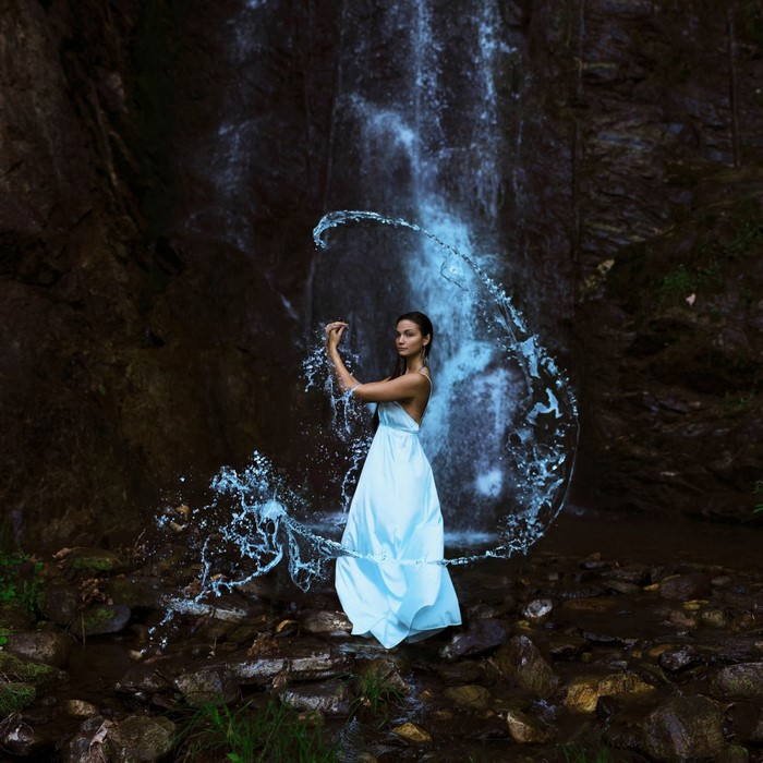 Woman in a light blue dress by a waterfall with water splashes