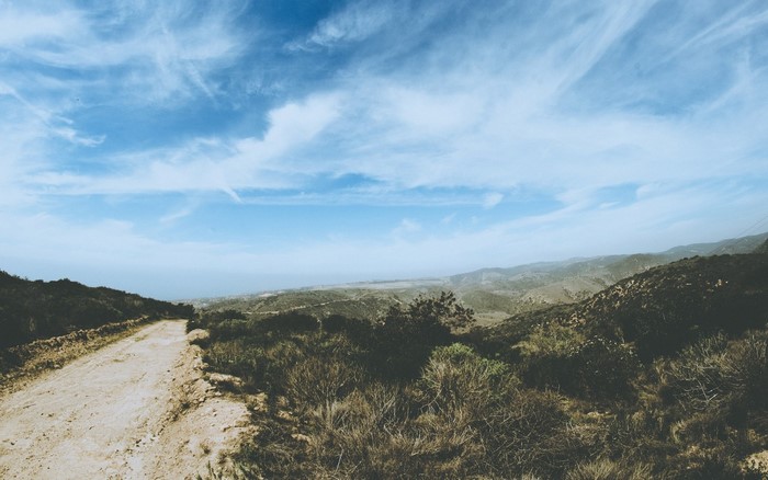 Dirt road leading to a valley with hills and the sea
