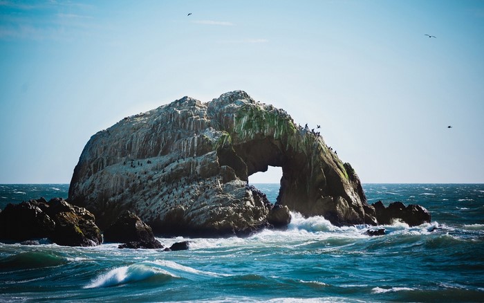 Rock formation with arch in the sea with birds