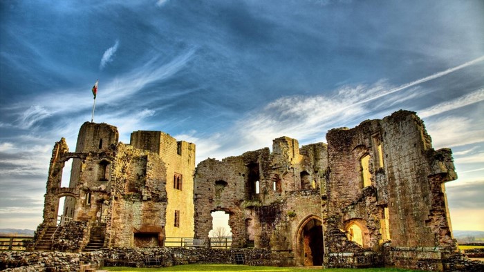 Ruins of a stone castle with a flag under a cloudy sky