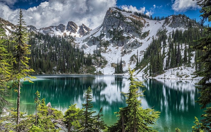 Turquoise lake reflecting snow-capped mountains and pine trees