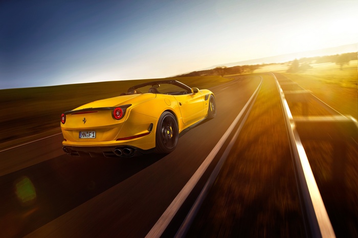 Yellow Ferrari California T driving on a road at sunset