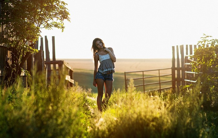 Young Woman in Jean Shorts Standing in Sunlit Meadow