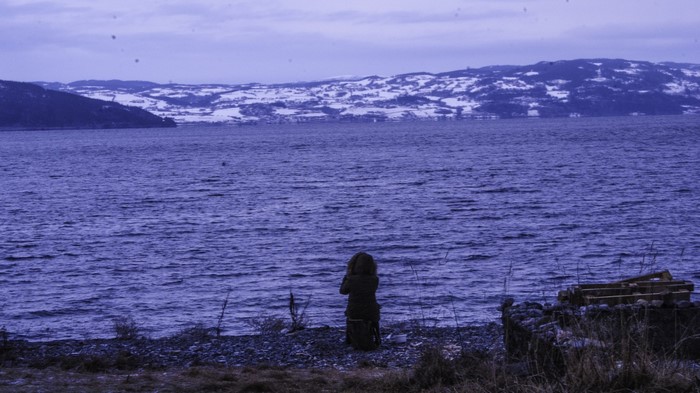 Person by a lake with snow-covered hills
