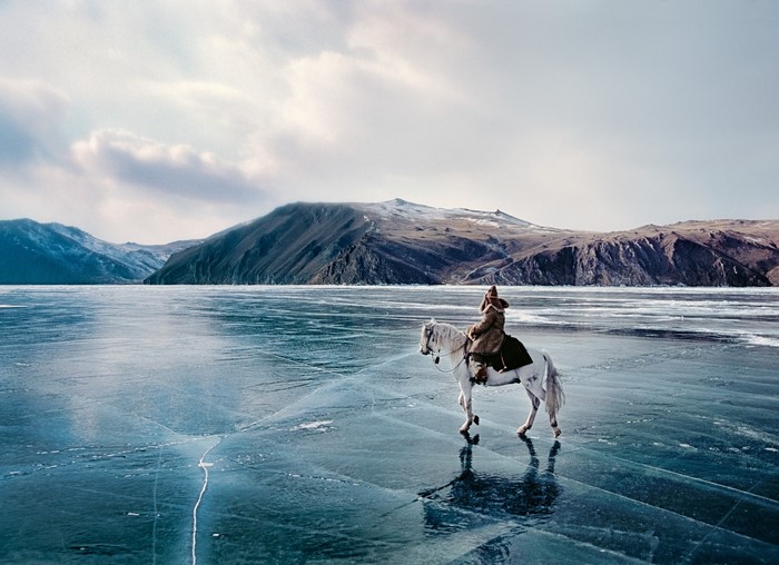 Person riding a white horse on frozen lake with mountains