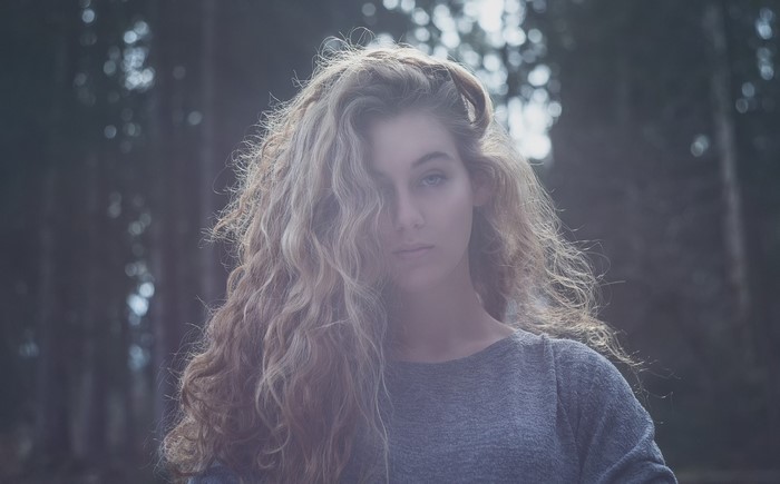 Woman with long curly blonde hair in a grey sweater outdoors