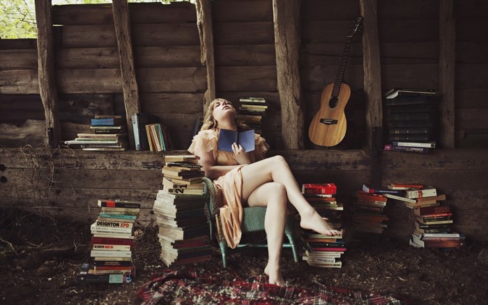Woman reading a book in a rustic setting with books and guitar