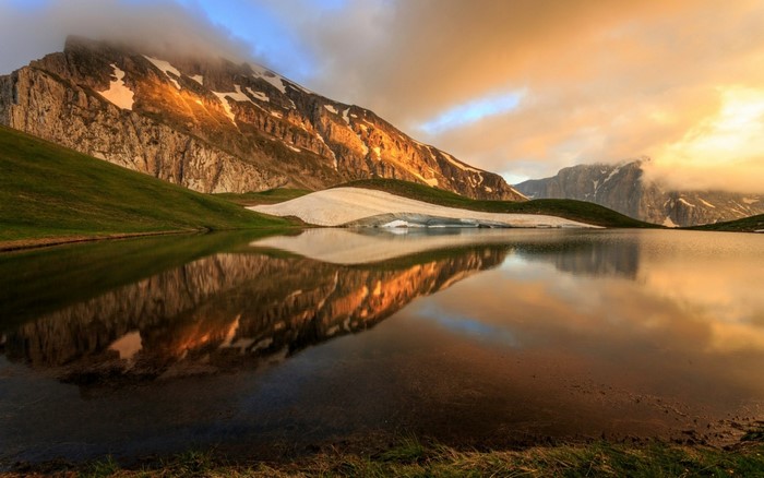 Mountain lake reflection at sunset with snow and clouds